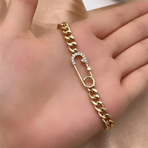 Detailed close-up of a gold Cuban chain bracelet with a crystal safety pin and star pendant