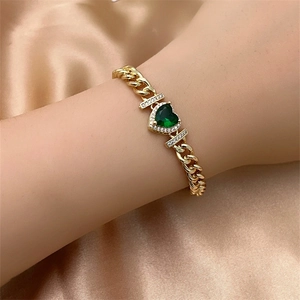 Detail of a gold Cuban link bracelet featuring a heart-shaped green gemstone with pavé stones