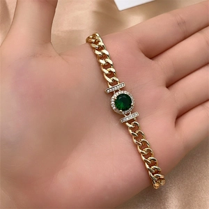 Close-up of gold Cuban chain bracelet with emerald green stone and sparkling micro-inlay