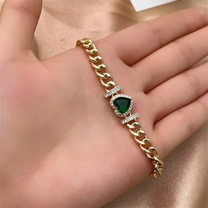 Macro shot of gold-plated Cuban chain bracelet with heart-shaped green gemstone