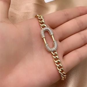 Detail of gold Cuban chain bracelet featuring a rhinestone encrusted oval link on wrist