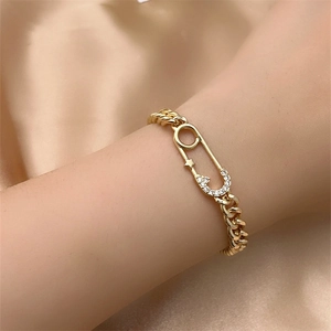 Detail of gold Cuban link bracelet featuring a safety pin pendant with inlaid zircon stars