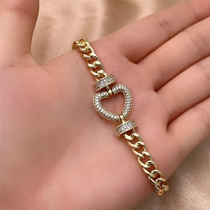 Macro shot of gold Cuban chain bracelet with zircon heart charm on silk background