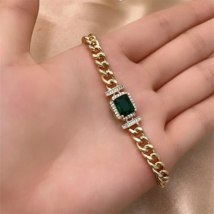 Close-up of gold Cuban chain bracelet featuring a green gemstone and micro-pave crystals