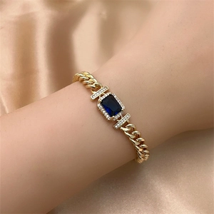 Detailed close-up of a gold Cuban chain bracelet with a rectangular blue gemstone and pavé