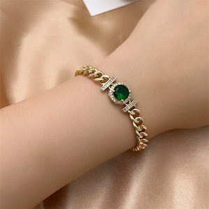 Close-up of gold cuban link bracelet with green stone on golden satin background