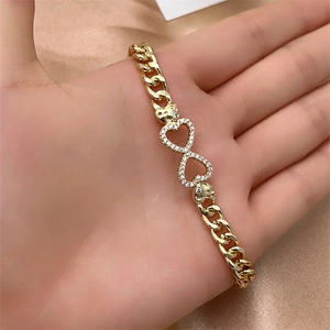 Detail of gold Cuban chain bracelet featuring pavé-set double hearts on satin background