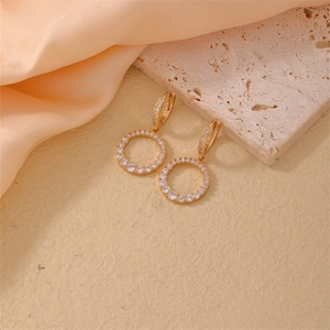 Boucles d'oreilles créoles dorées géométriques avec zircons brillants sur fond travertin