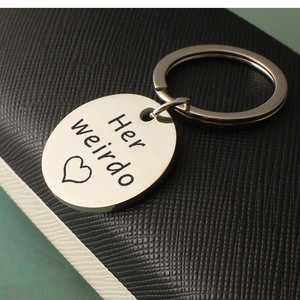 Detail of Her Weirdo engraved stainless steel keychain on black leather background