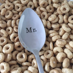 Close-up of polished stainless steel spoon engraved with Mr and heart on cereal background