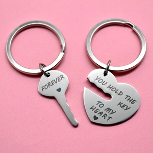Polished stainless steel couple keychains with heart and key pendants on pink background