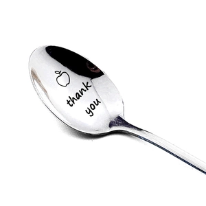 Close-up of polished stainless steel spoon with thank you engraving and apple motif