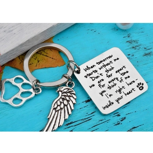 Dog memorial keychain with angel wing and heart paw charm on blue wooden surface