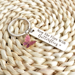 Silver butterfly keychain with Now She Flies With Butterflies engraved tag on straw mat