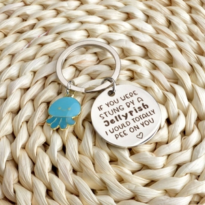 Detail of blue jellyfish keychain with humorous engraved stainless steel charm on straw mat