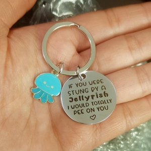 Detail view of a metal jellyfish keychain featuring engraved text and a blue charm
