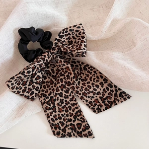 Detailed close-up of a leopard print silk bow hair scrunchie on beige linen fabric background