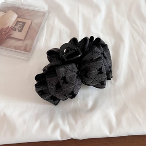 Close-up of a large tweed bow hair claw clip in dark grey with star texture on white fabric