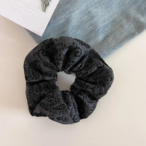 Close-up of black wool paisley pattern scrunchie hair tie on denim background
