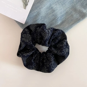 Detailed view of a vintage dark blue paisley scrunchie made of wool fabric on a white desk
