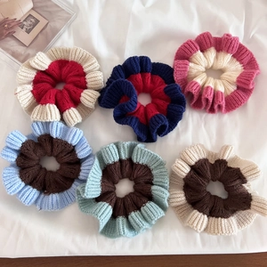 Detail view of six knit scrunchies in varied color-block designs on a soft fabric