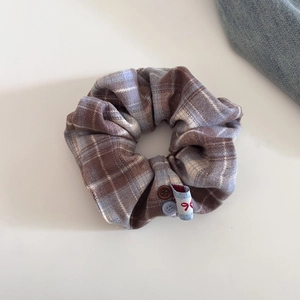 Detailansicht eines Retro-Karo-Haargummis mit Knopfablikationen und Schleifenetikett