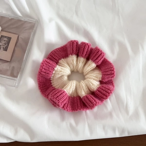 Close-up of pink and white knitted scrunchie with spiral texture on a soft white cloth
