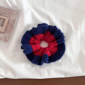 Detail shot of a contrast color knit scrunchie with red and navy blue ruffle textures