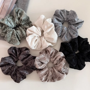 Close-up of six premium velvet scrunchies in neutral colors like green and khaki