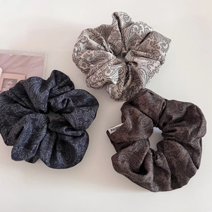 Detailed view of paisley scrunchies in black, grey, and coffee on a minimalist white backdrop