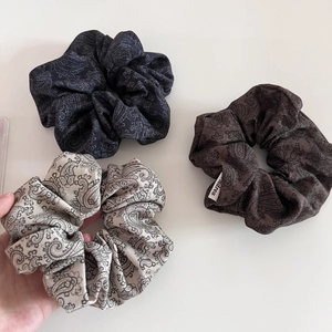 Detail of three paisley print scrunchies in black, brown, and beige fabric textures