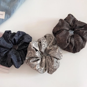 Close-up of paisley pattern scrunchies in navy blue, light gray, and deep brown tones