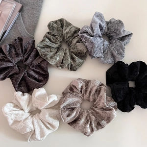 Close-up of six soft velvet scrunchies in classic autumn colors on a neutral background