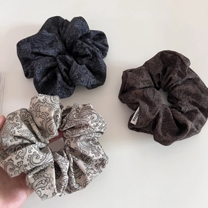 Close-up of retro paisley scrunchies in navy, coffee, and beige with brand tag detail