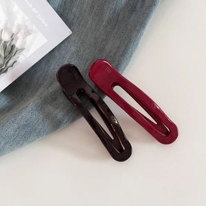 Detail view of long acetate hair clips in deep brown and berry red with handmade engraving