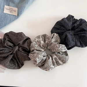 Close-up of three paisley silk-texture scrunchies in brown, cream, and charcoal colors
