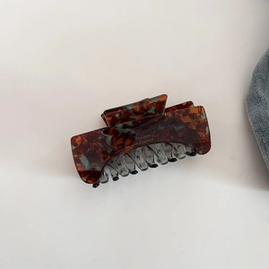 Detail of tortoise shell claw clip with gold lettering on a minimalist background