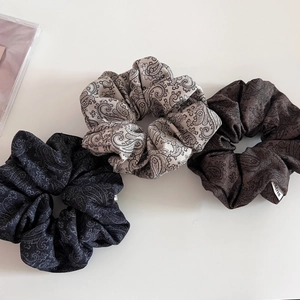 Detailed view of three paisley print scrunchies in grey and brown textured fabric