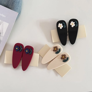 Three pairs of floral acetate hair clips in black, beige, and red on white cardstock