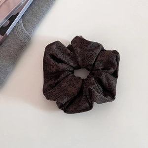 Macro detail of high-quality brown paisley pattern fabric scrunchie with pearly finish
