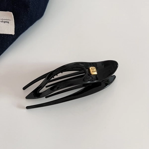 Détail d'une pince à cheveux noire brillante en forme d'hirondelle avec emblème doré