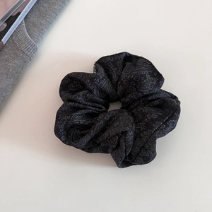 Detailed view of large black paisley jacquard scrunchie hair tie with silver patterns