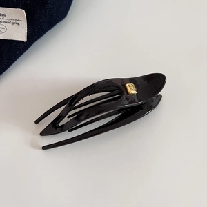 Détail d'une pince à cheveux noire brillante avec une plaque dorée fashion élégante