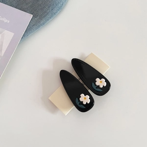 Detail of two black acetate flower hair clips with green leaves on white background