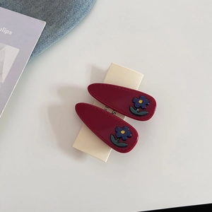 Detail shot of two dark red resin drop hair clips with blue flower accents on card