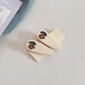 Detailed macro view of cream teardrop hair clips featuring brown floral relief patterns