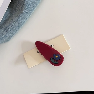 Detail of burgundy droplet hair clip with a cute 3D floral accent and stitching texture