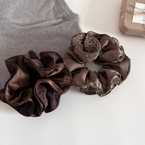 Detailed view of satin leopard print scrunchies set on a grey knit fabric background