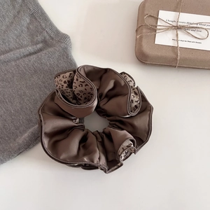 Brown satin scrunchie with leopard print trim and soft pleated texture for hair styling