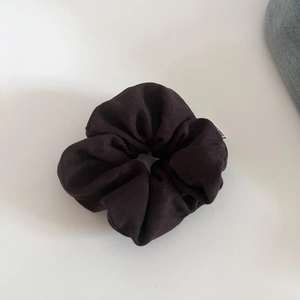 Detailed view of dark brown textured fabric scrunchie with visible woven texture and white label